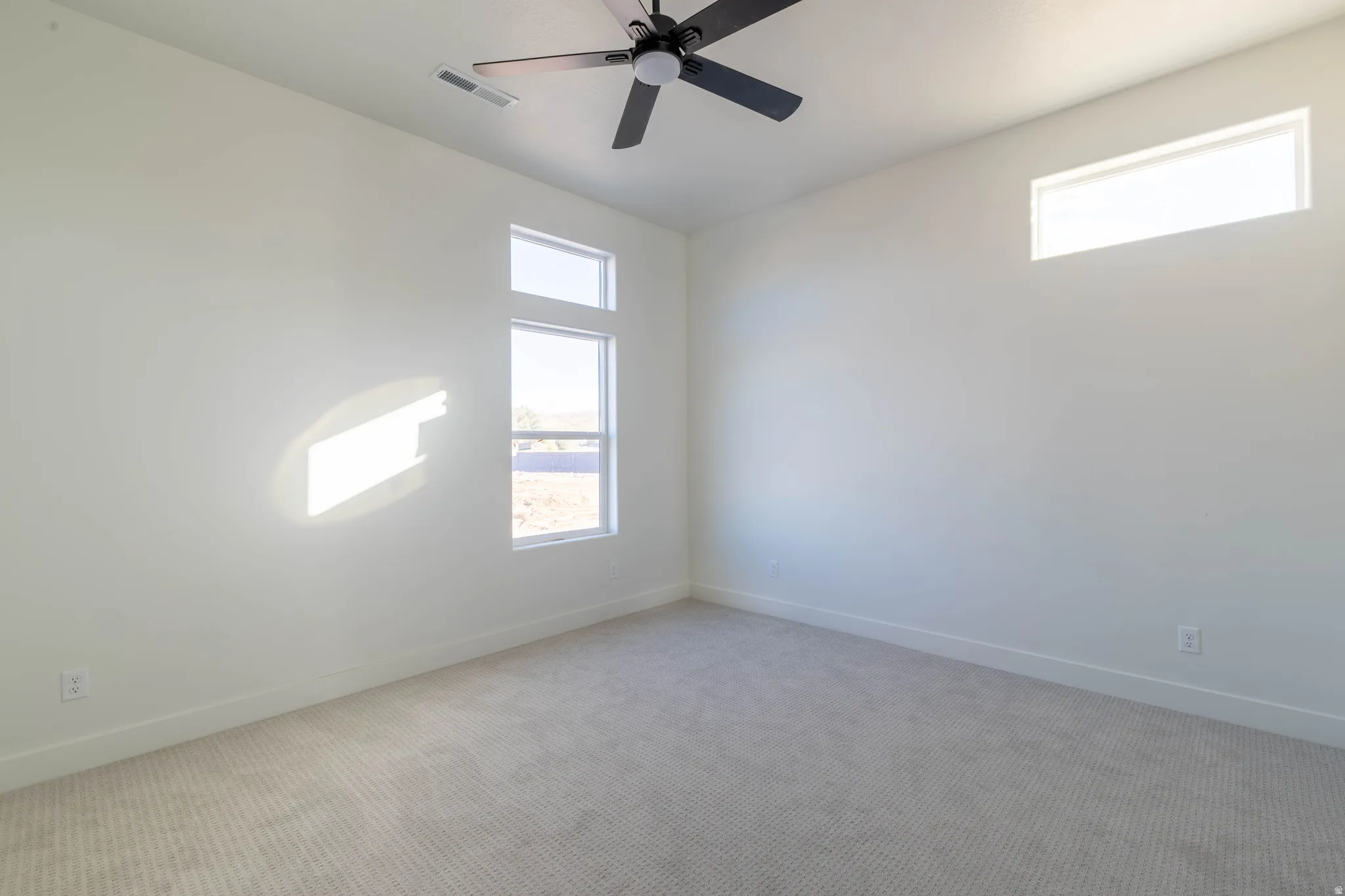 Carpeted spare room with plenty of natural light and a ceiling fan