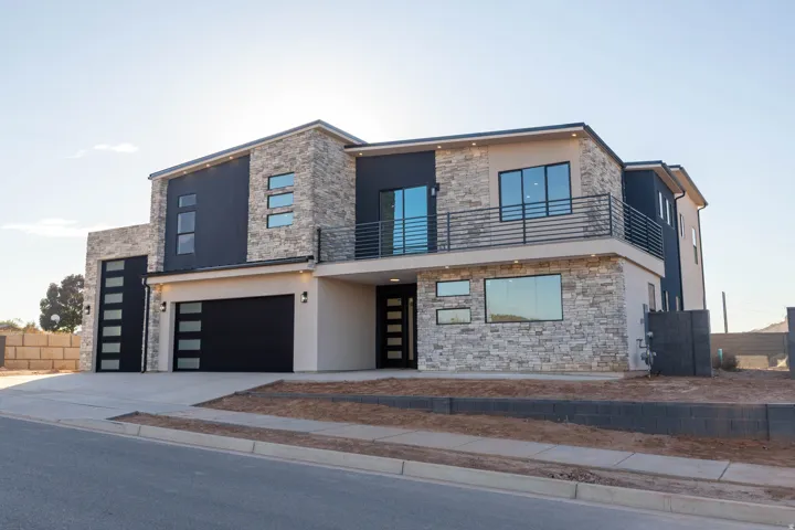 Contemporary home featuring stone siding, stucco siding, concrete driveway, and a balcony