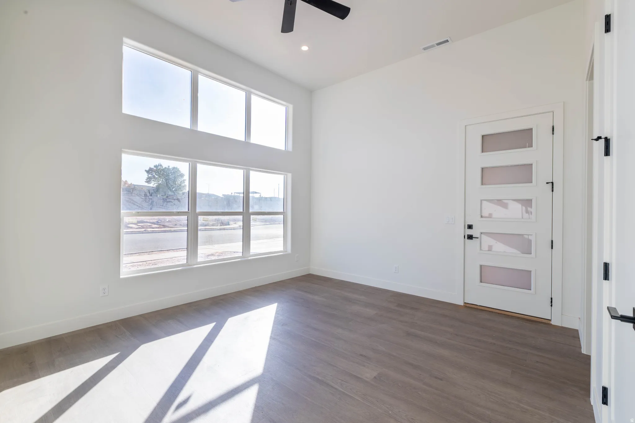 Unfurnished room with dark wood-style flooring, a ceiling fan, and a high ceiling
