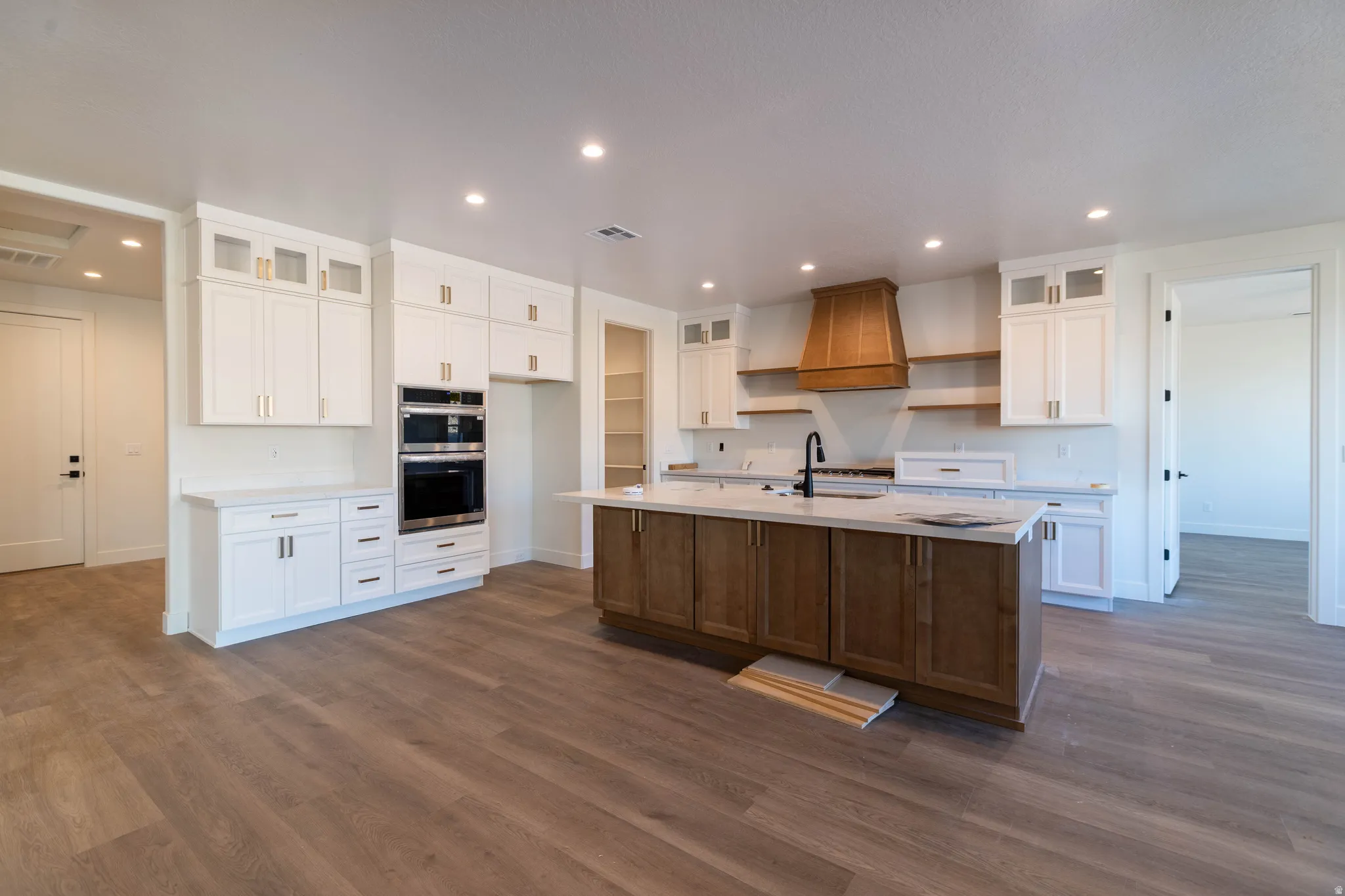 Kitchen with glass insert cabinets, open shelves, white cabinets, an island with sink, and stainless steel double oven