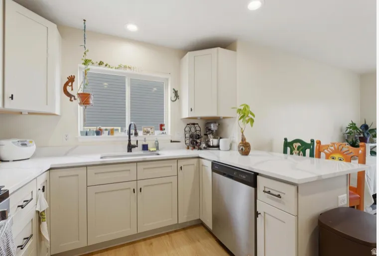Kitchen with dishwasher, light wood-type flooring, a peninsula, light stone counters, and recessed lighting