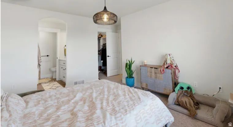 Bedroom featuring a walk in closet, arched walkways, light carpet, and ensuite bath