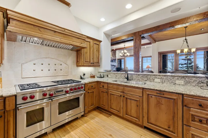 Gourmet kitchen featuring a professional-grade stainless steel range with double ovens, a matching wood-paneled vent hood, and natural wood cabinetry