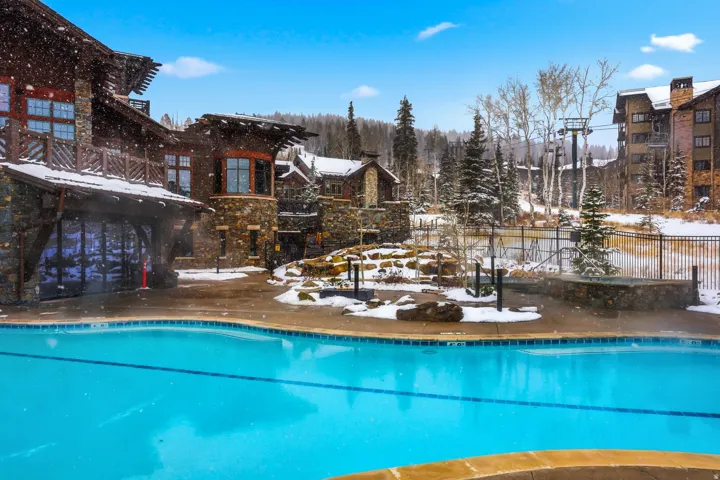 Outdoor swimming pool with tiled perimeter, surrounded by extensive stone and wood-clad structures