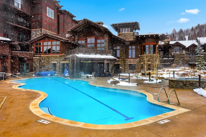 Curved outdoor swimming pool with integrated hot tub, surrounded by a concrete deck with stone accents