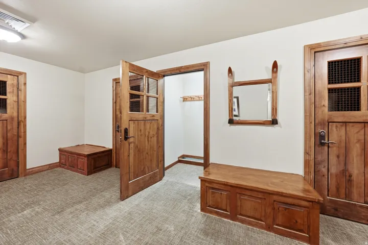 Entryway featuring natural wood doors with grated window panes, light-toned carpeting, and a built-in wood bench with storage