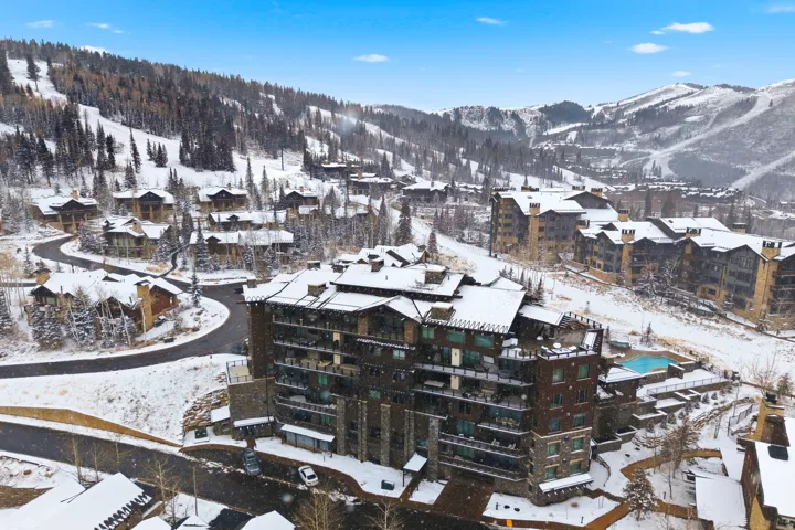 Multistory building featuring stone and timber-style exterior finishes, multiple private balconies, and a built-in outdoor pool