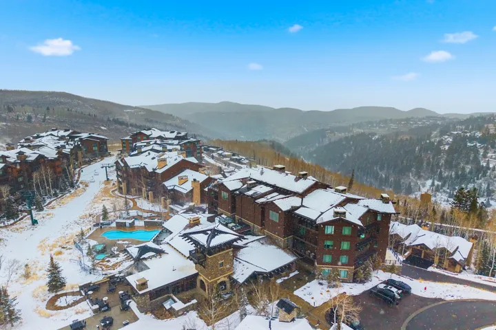 Mountain resort community featuring multiple buildings with snow-covered roofs, a visible ski slope, and an outdoor pool area