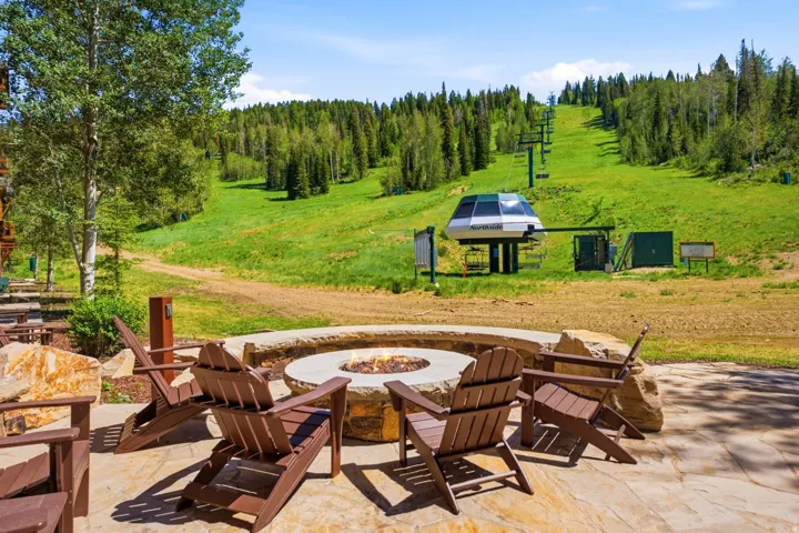 Flagstone patio featuring a built-in stone fire pit, surrounded by green hillside and mature trees