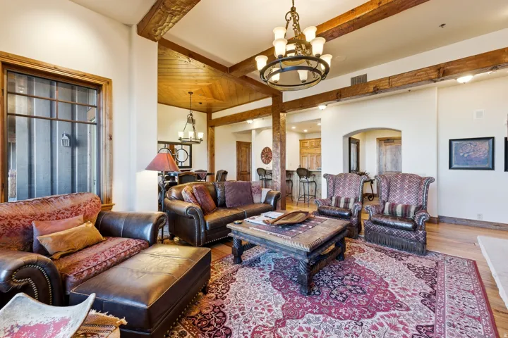 Spacious living area featuring exposed wood ceiling beams, hardwood flooring, and a large central chandelier
