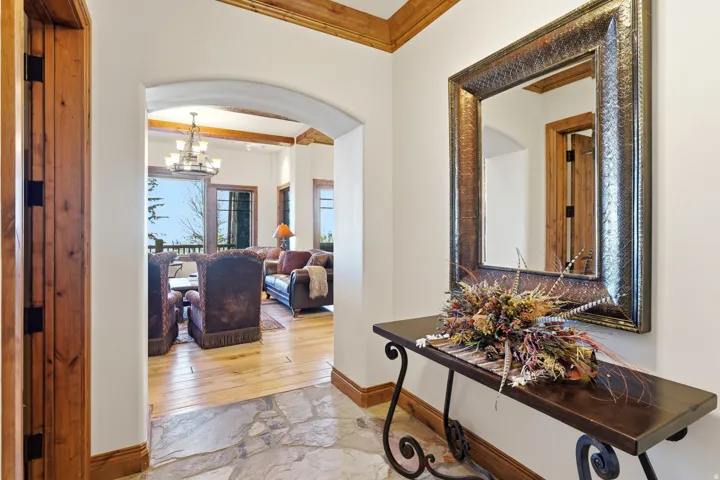 Foyer featuring flagstone flooring, a decorative arched entry, a wood-framed mirror, and a wood-finish console table, opening to a living area with wood-finish flooring and exposed beam ceilings
