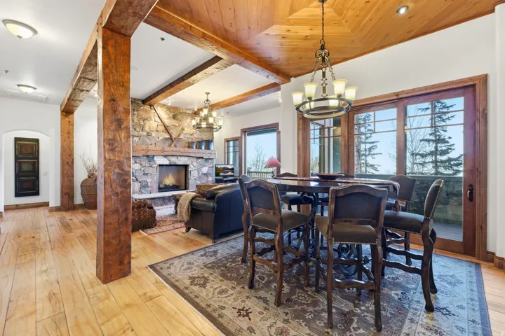 Living area featuring exposed wooden beams, a stone fireplace, wood-finish flooring, a wood-paneled ceiling, and large sliding glass doors