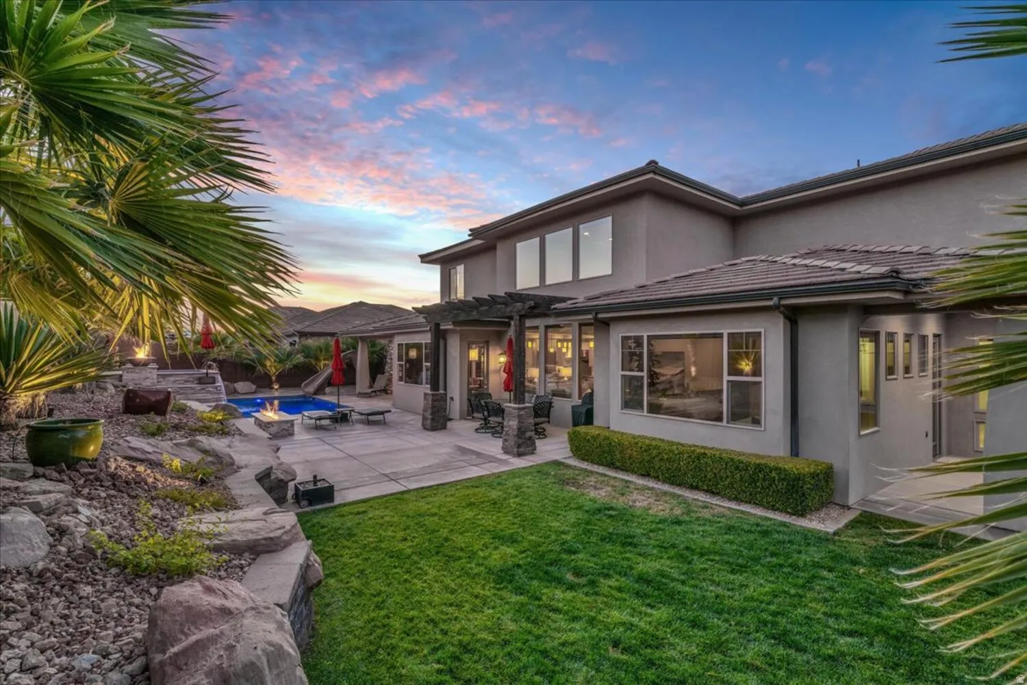 Back of house at dusk with stucco siding, a pergola, a lawn, an outdoor pool, and a patio