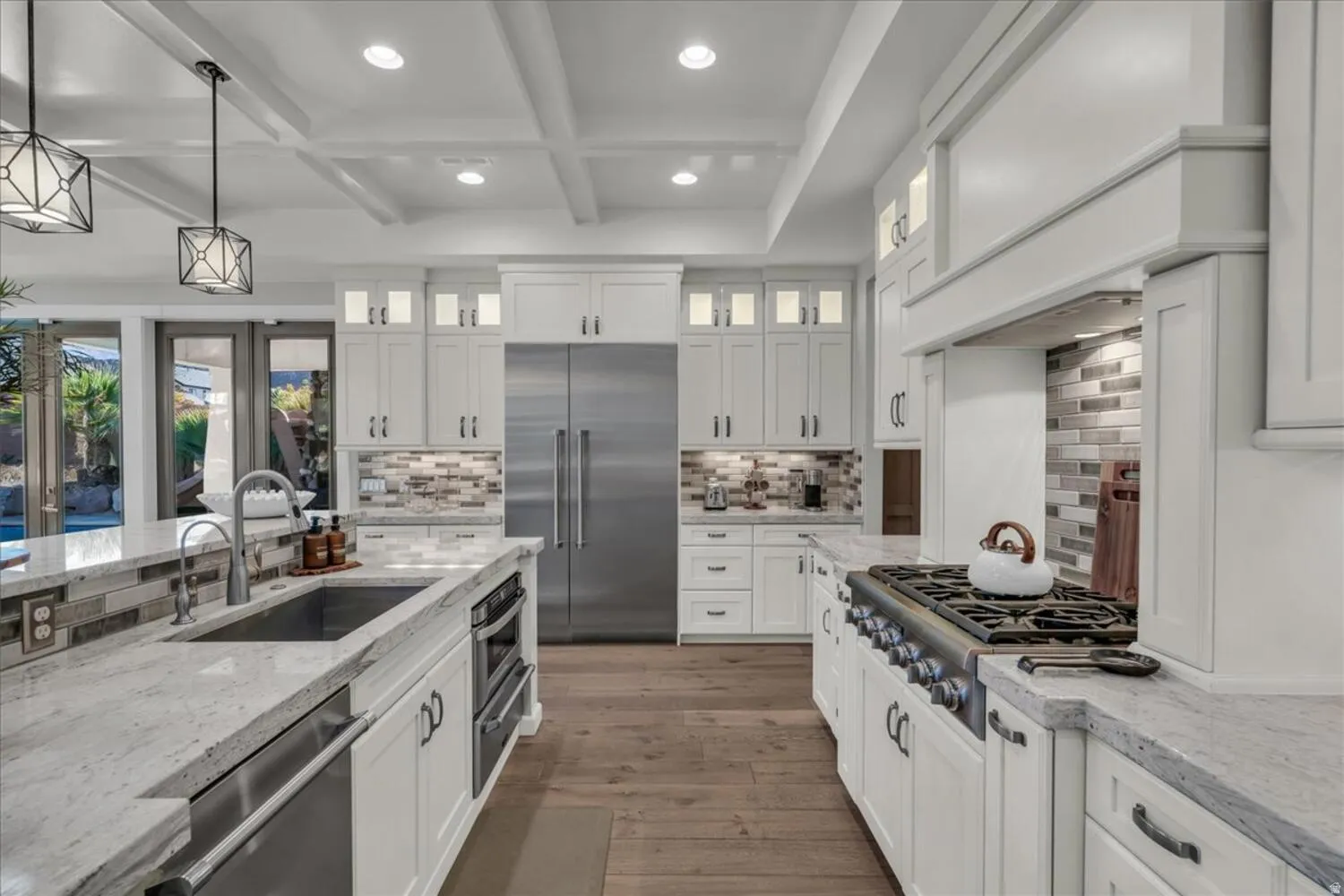 Kitchen with light stone countertops, appliances with stainless steel finishes, hanging light fixtures, beamed ceiling, and white cabinets
