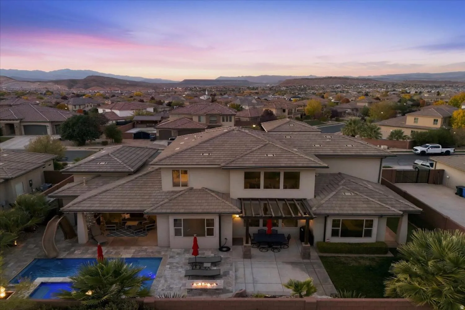 Back of property at dusk featuring a residential view, outdoor dining area, stucco siding, an outdoor fire pit, and a patio area