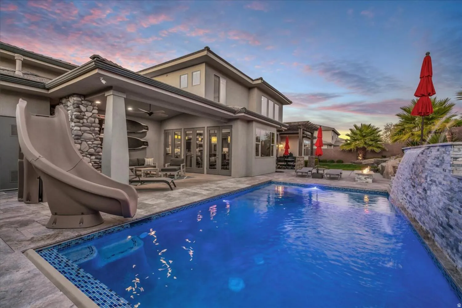 Pool at dusk with an outdoor pool, a patio area, a water slide, an outdoor hangout area, and french doors