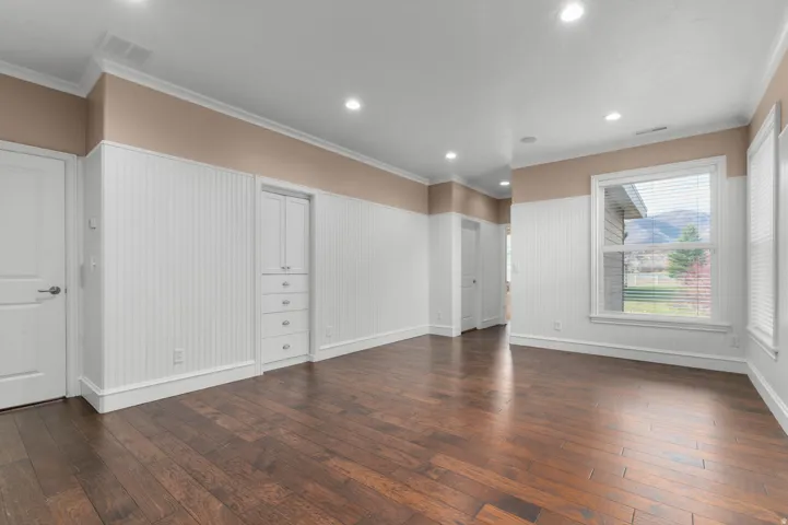 Empty room featuring ornamental molding, dark wood-style flooring, recessed lighting, and wainscoting