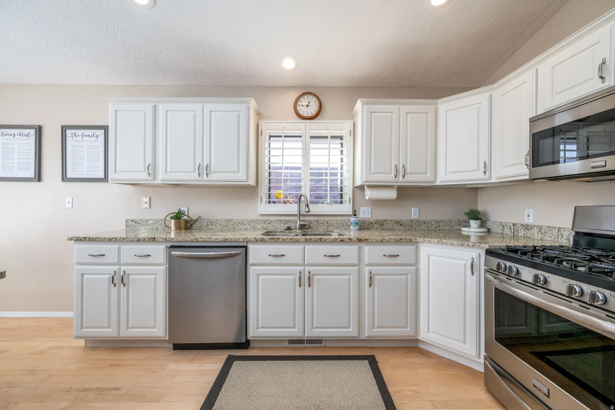 Kitchen with stainless steel appliances, white cabinetry, light wood-type flooring, light stone counters, and a textured ceiling