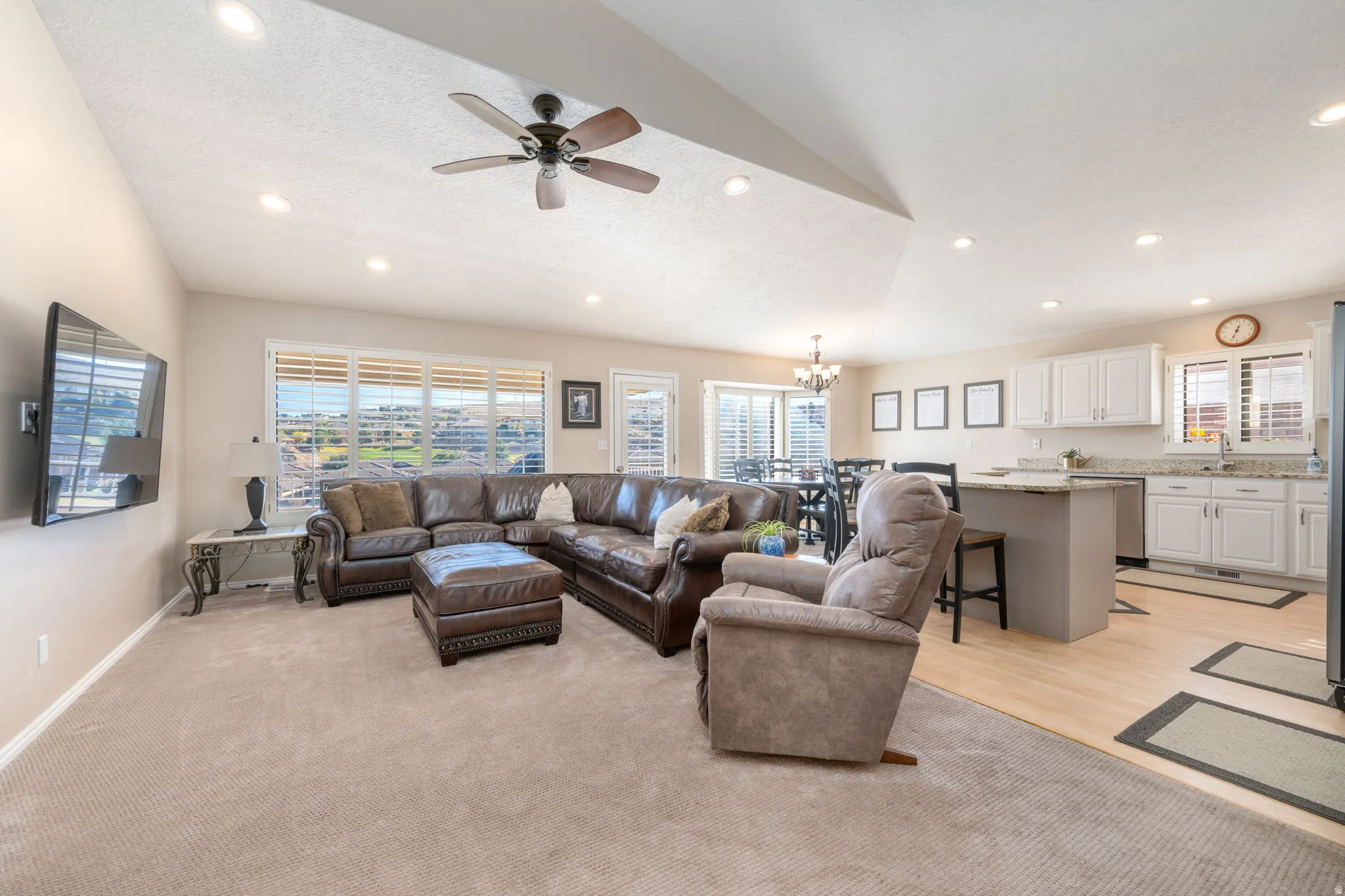 Living room with a chandelier, lofted ceiling, a ceiling fan, light carpet, and plenty of natural light