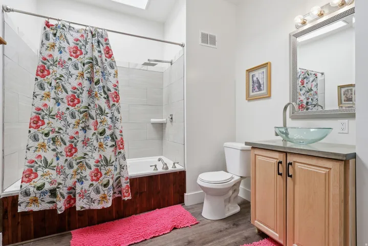 Bathroom with vanity, shower / tub combo with curtain, wood finished floors, and a skylight