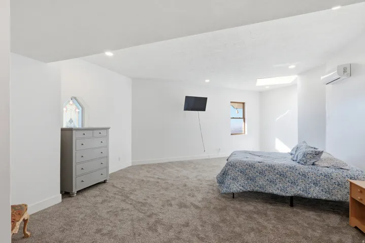Bedroom with light carpet, a wall mounted air conditioner, recessed lighting, and a textured ceiling