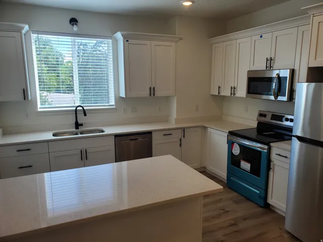 Kitchen with stainless steel appliances, white cabinetry, light stone countertops, and dark wood-style flooring