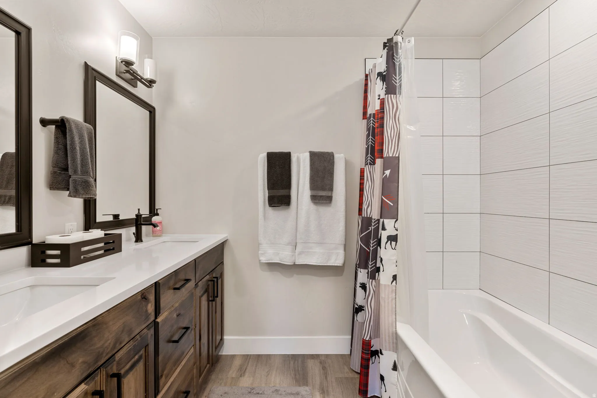 Full bath featuring double vanity, shower / bathtub combination with curtain, and light wood-style floors