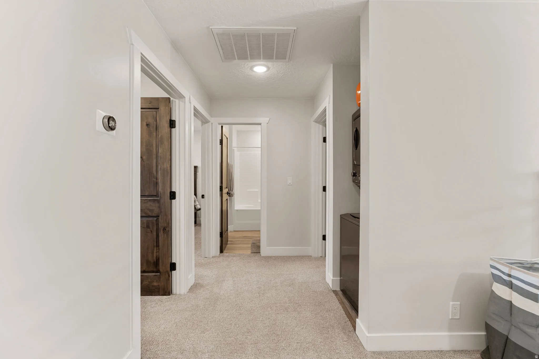 Hallway with stacked washing machine and dryer and light carpet