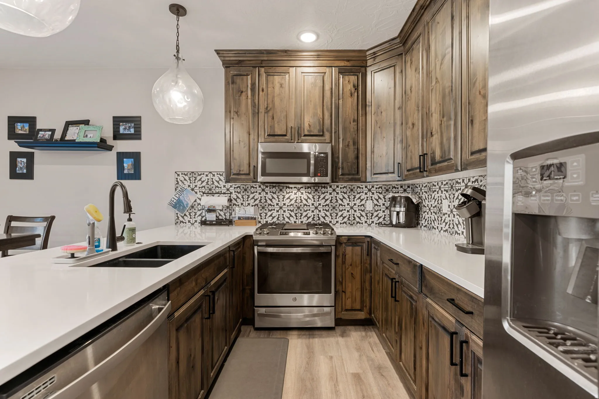 Kitchen with appliances with stainless steel finishes, hanging light fixtures, dark brown cabinetry, backsplash, and light wood finished floors