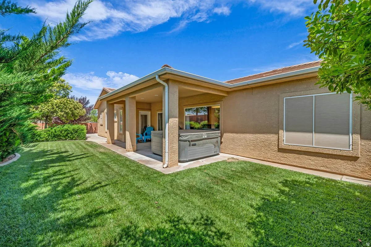 Back of property featuring a hot tub, stucco siding, a patio area, and a yard