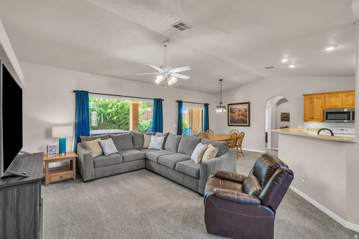 Living room with carpet, arched walkways, vaulted ceiling, and ceiling fan