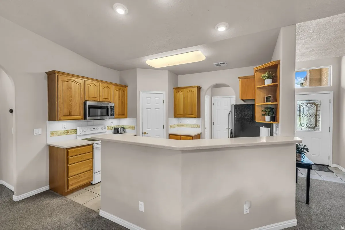 Kitchen with arched walkways, brown cabinets, light countertops, stainless steel appliances, and light tile patterned floors