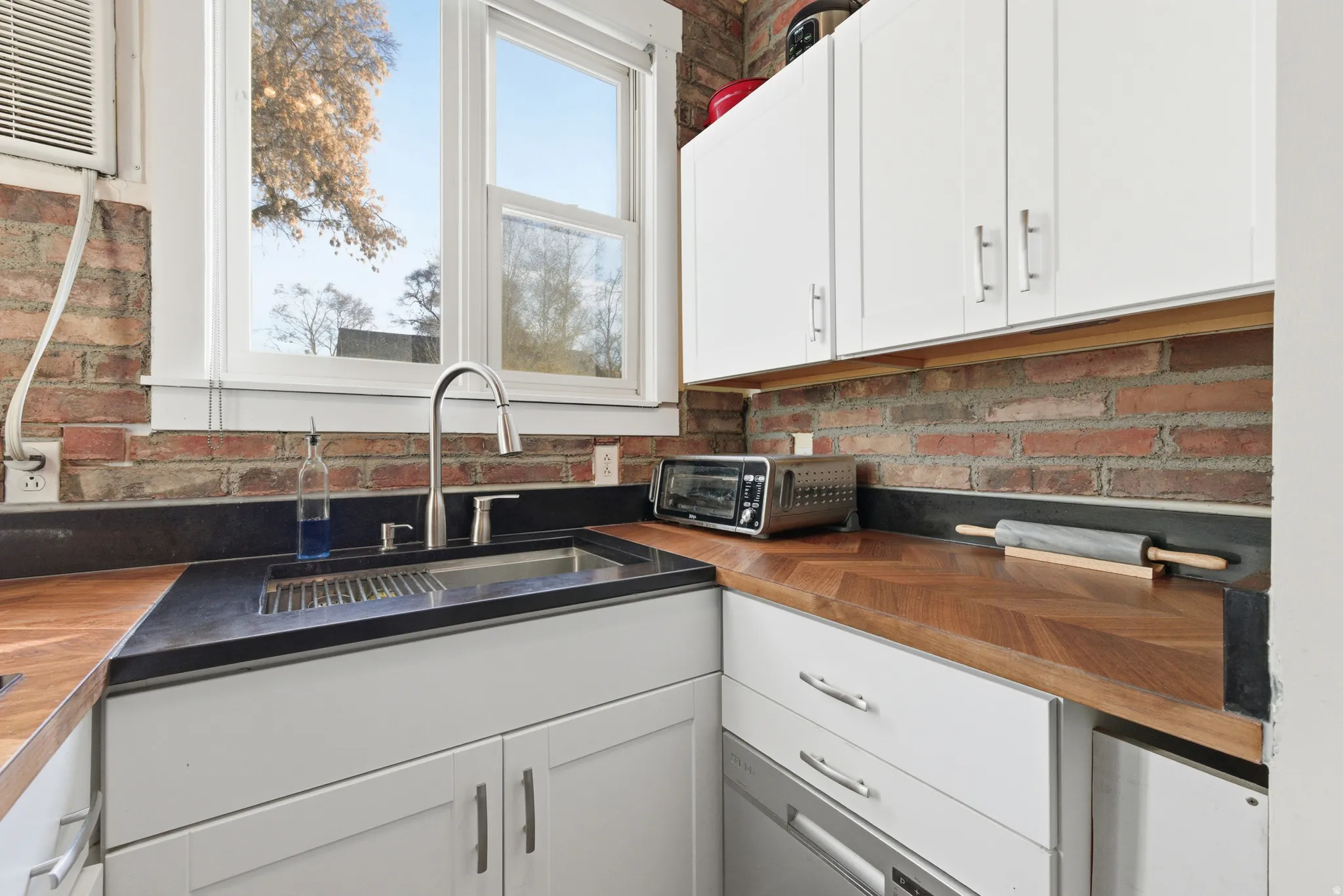Kitchen with butcher block counters, white cabinets, and a wall unit AC