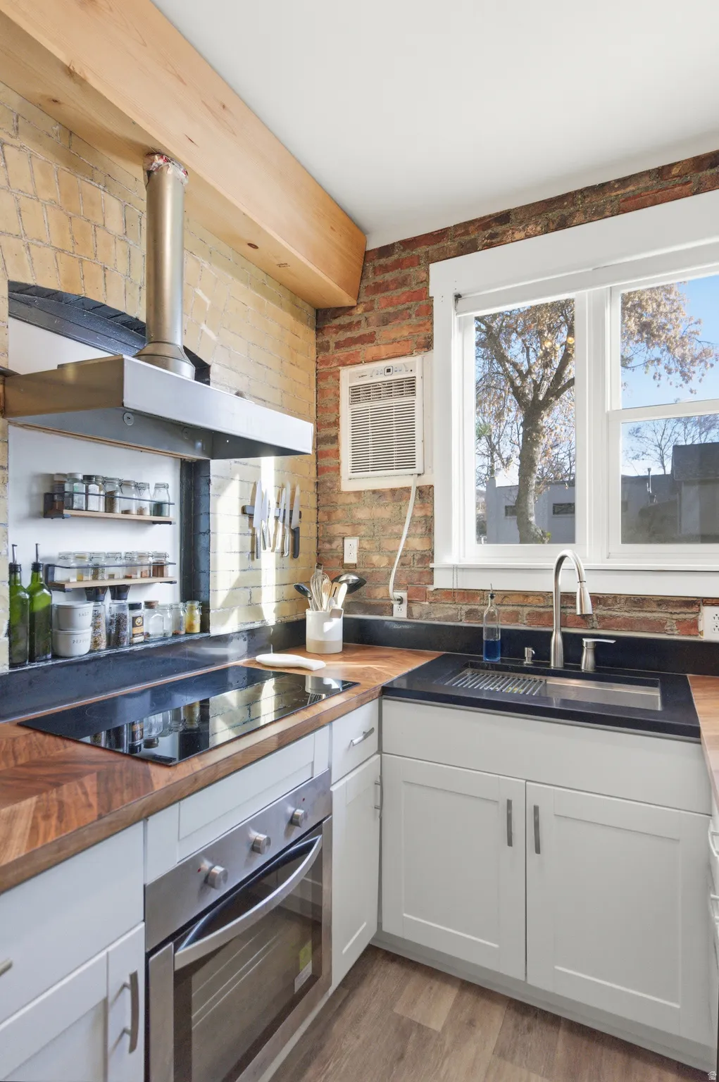 Kitchen featuring wood counters, white cabinetry, stainless steel oven, black electric cooktop, and wall chimney range hood