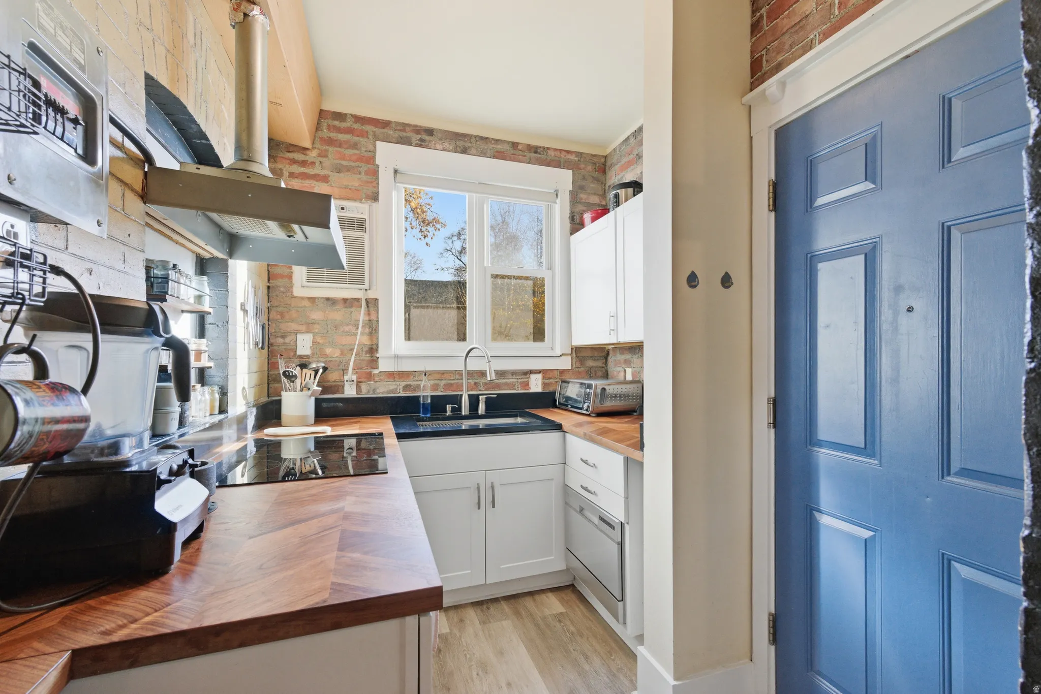 Kitchen featuring butcher block counters, white cabinetry, wall chimney range hood, tasteful backsplash, and light wood-style flooring