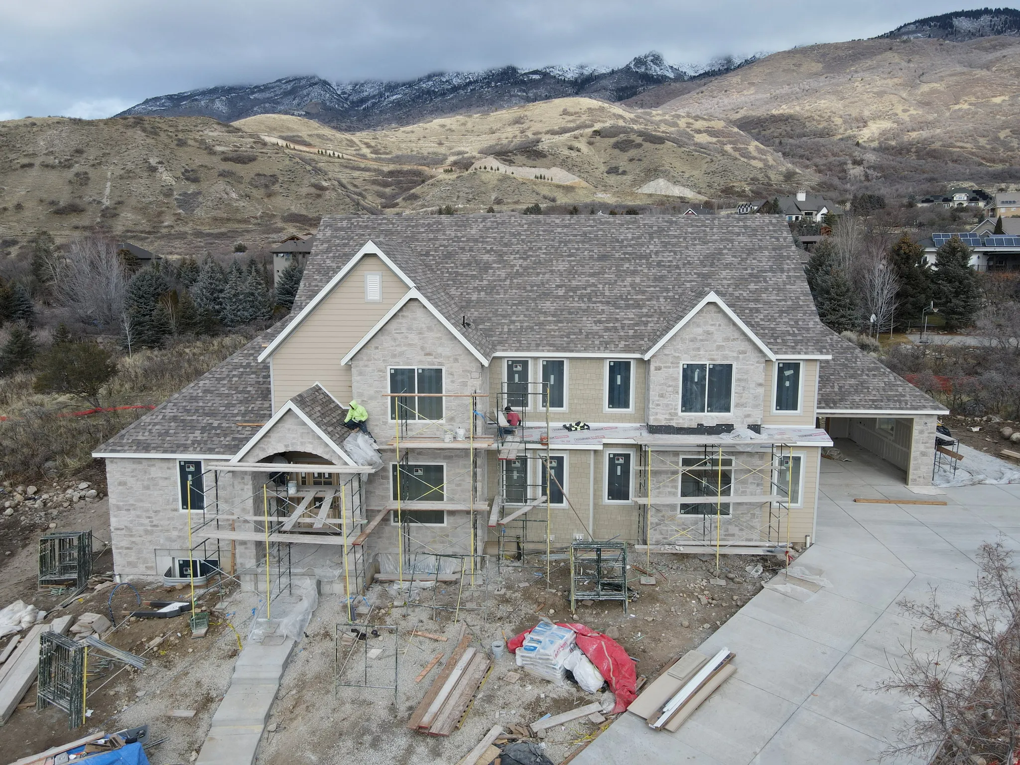 Unfinished property with a mountain view, a balcony, roof with shingles, and stone siding