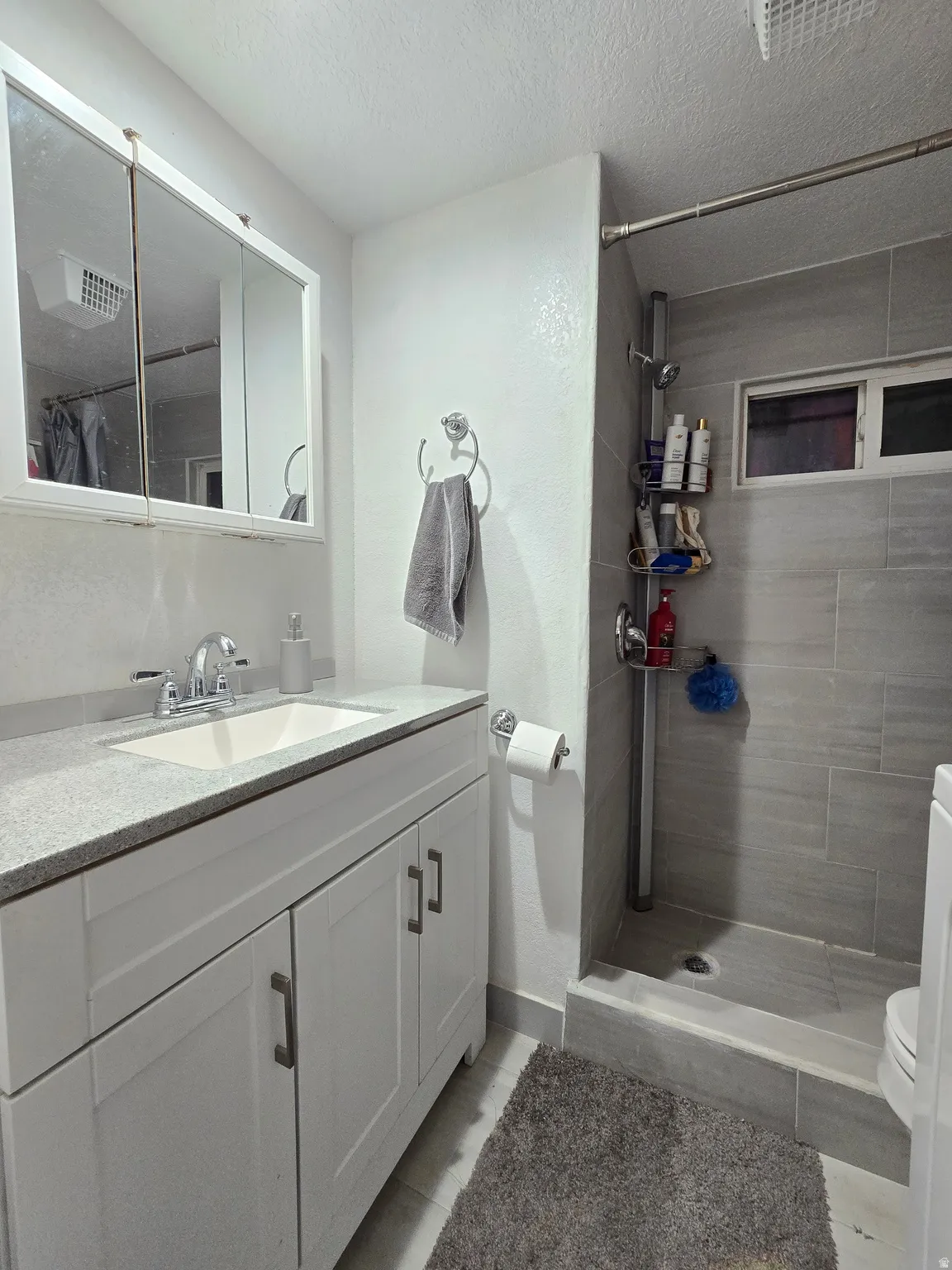 Bathroom featuring vanity, a tile shower, a textured ceiling, and light tile patterned floors