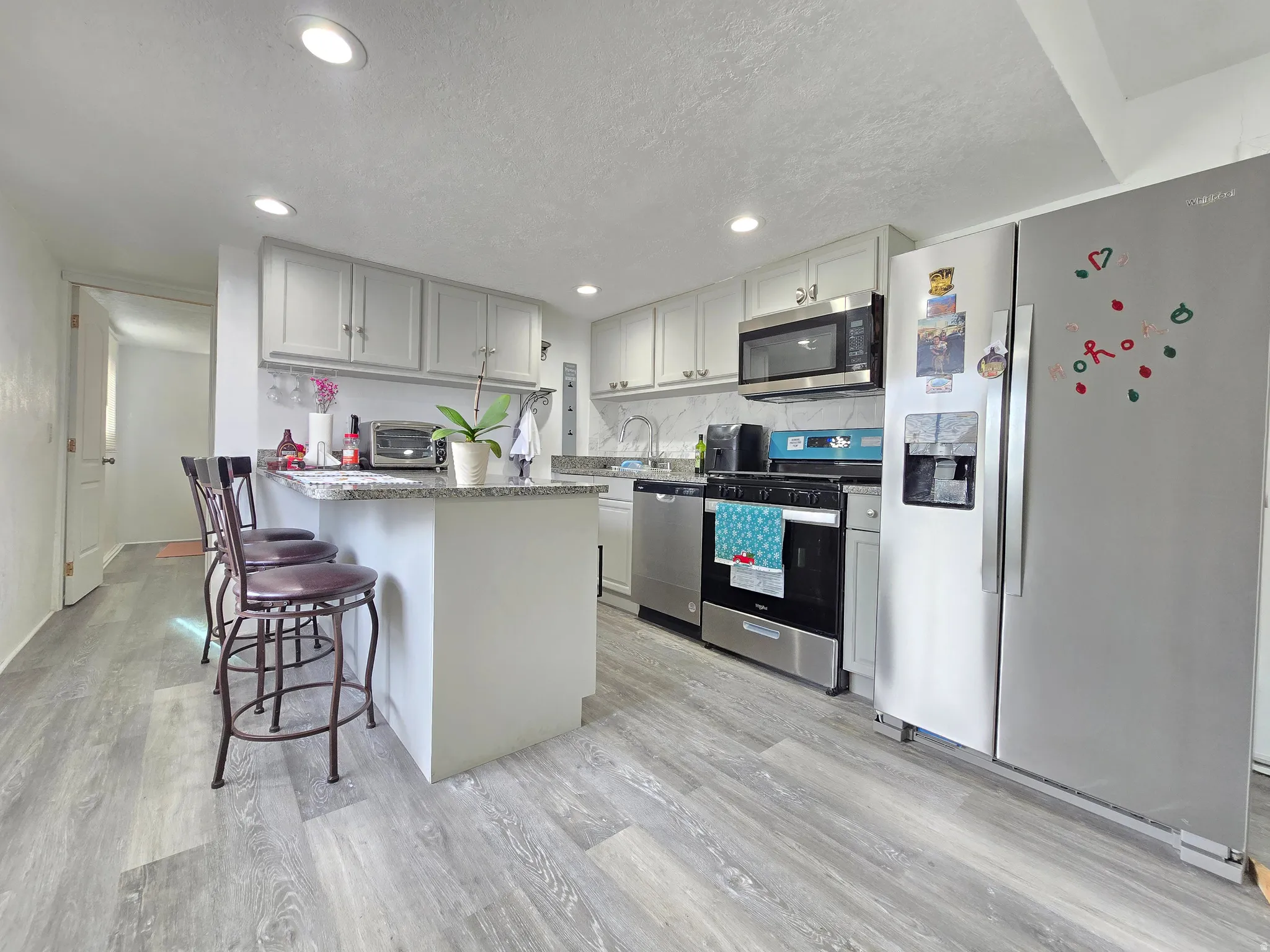 Kitchen with appliances with stainless steel finishes, a kitchen bar, a textured ceiling, a peninsula, and light stone countertops