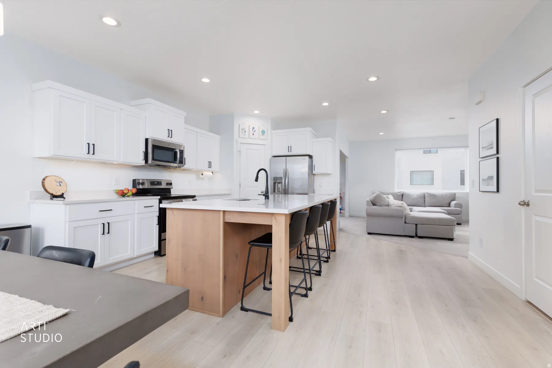 Kitchen featuring a kitchen breakfast bar, white cabinets, stainless steel appliances, a kitchen island with sink, and recessed lighting