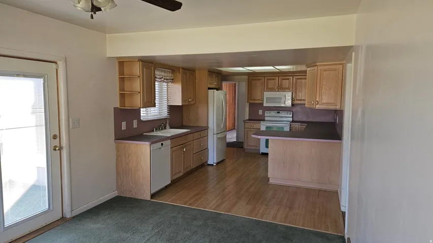 Kitchen with open shelves, white appliances, light carpet, a peninsula, and dark countertops