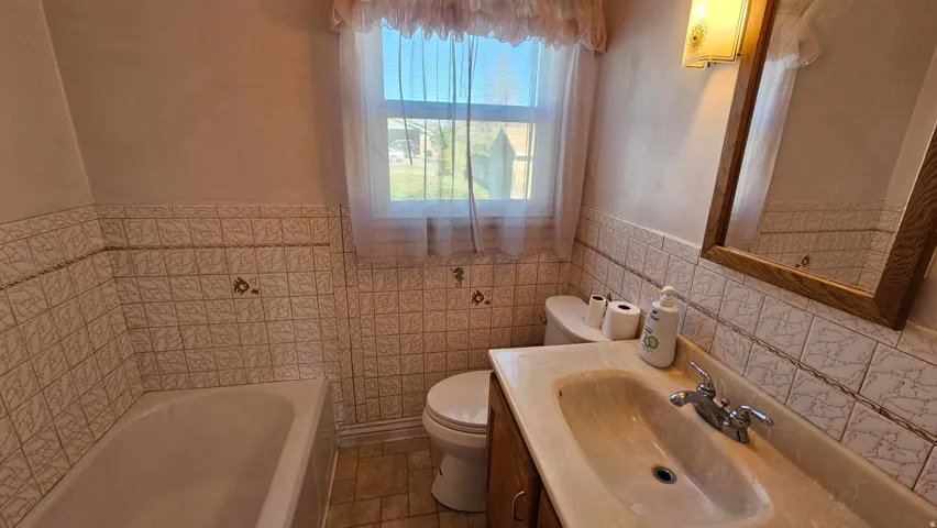 Full Bathroom with a garden tub, vanity, wainscoting, and tile walls