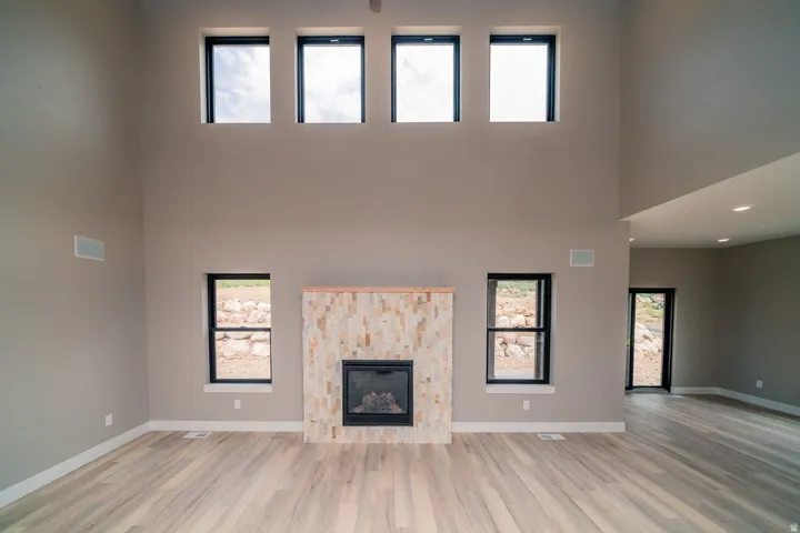 Unfurnished living room with a towering ceiling, a glass covered fireplace, and light wood-style floors