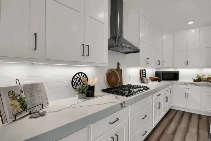 Kitchen featuring white cabinets, wall chimney range hood, light stone countertops, and stainless steel gas cooktop