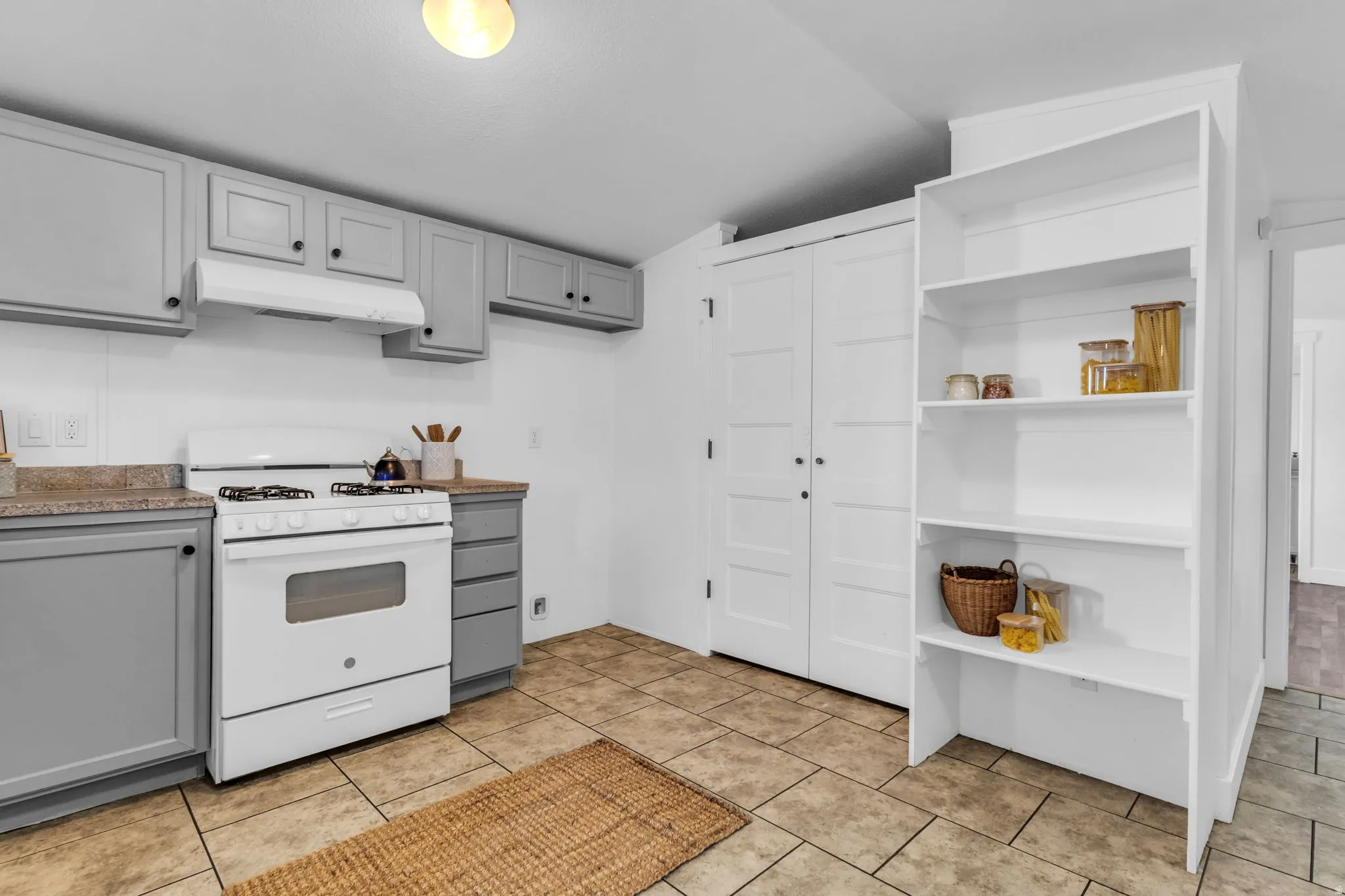 Kitchen featuring gray cabinets, white gas stove, under cabinet range hood, lofted ceiling, and light countertops