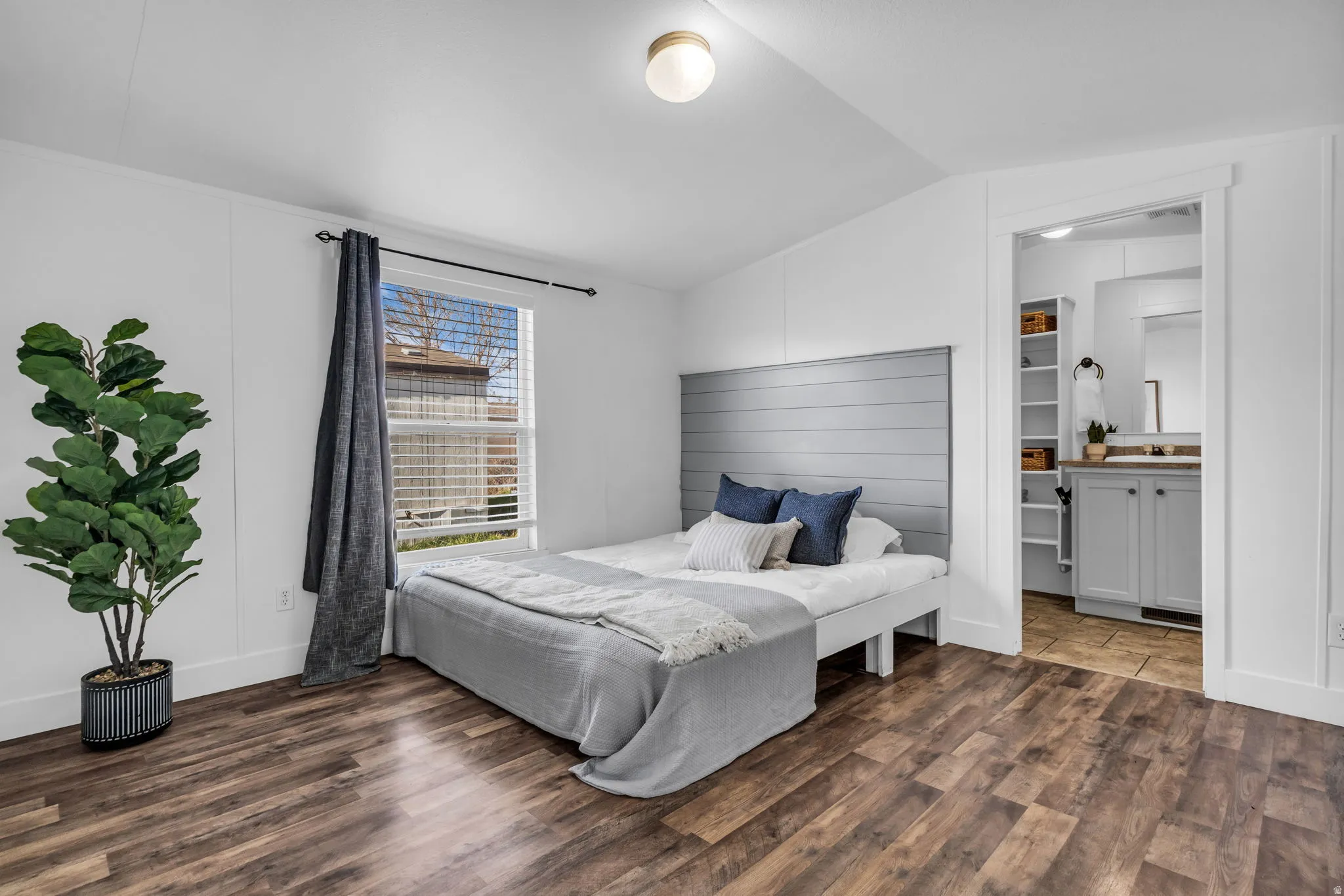 Bedroom with dark wood-style floors, vaulted ceiling, and connected bathroom