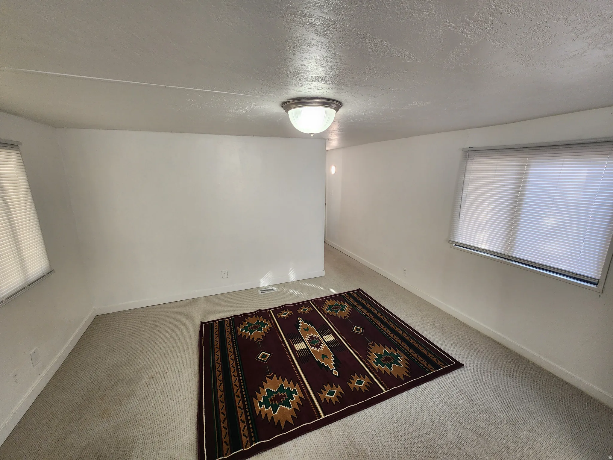Carpeted empty room with a textured ceiling and baseboards