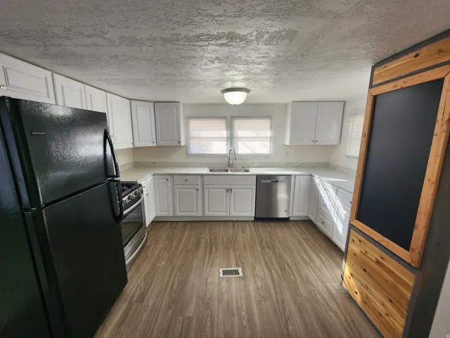 Kitchen with stainless steel appliances, white cabinetry, wood finished floors, and a textured ceiling