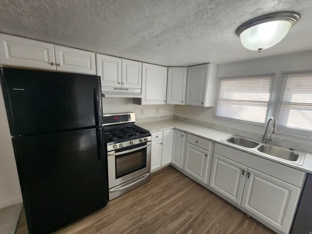 Kitchen featuring appliances with stainless steel finishes, white cabinets, a textured ceiling, dark wood-style flooring, and under cabinet range hood