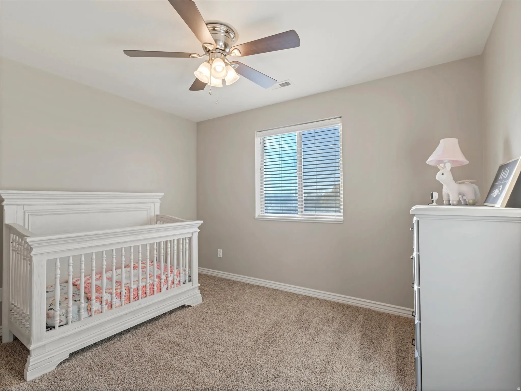 Bedroom featuring light colored carpet, ceiling fan, and a nursery area