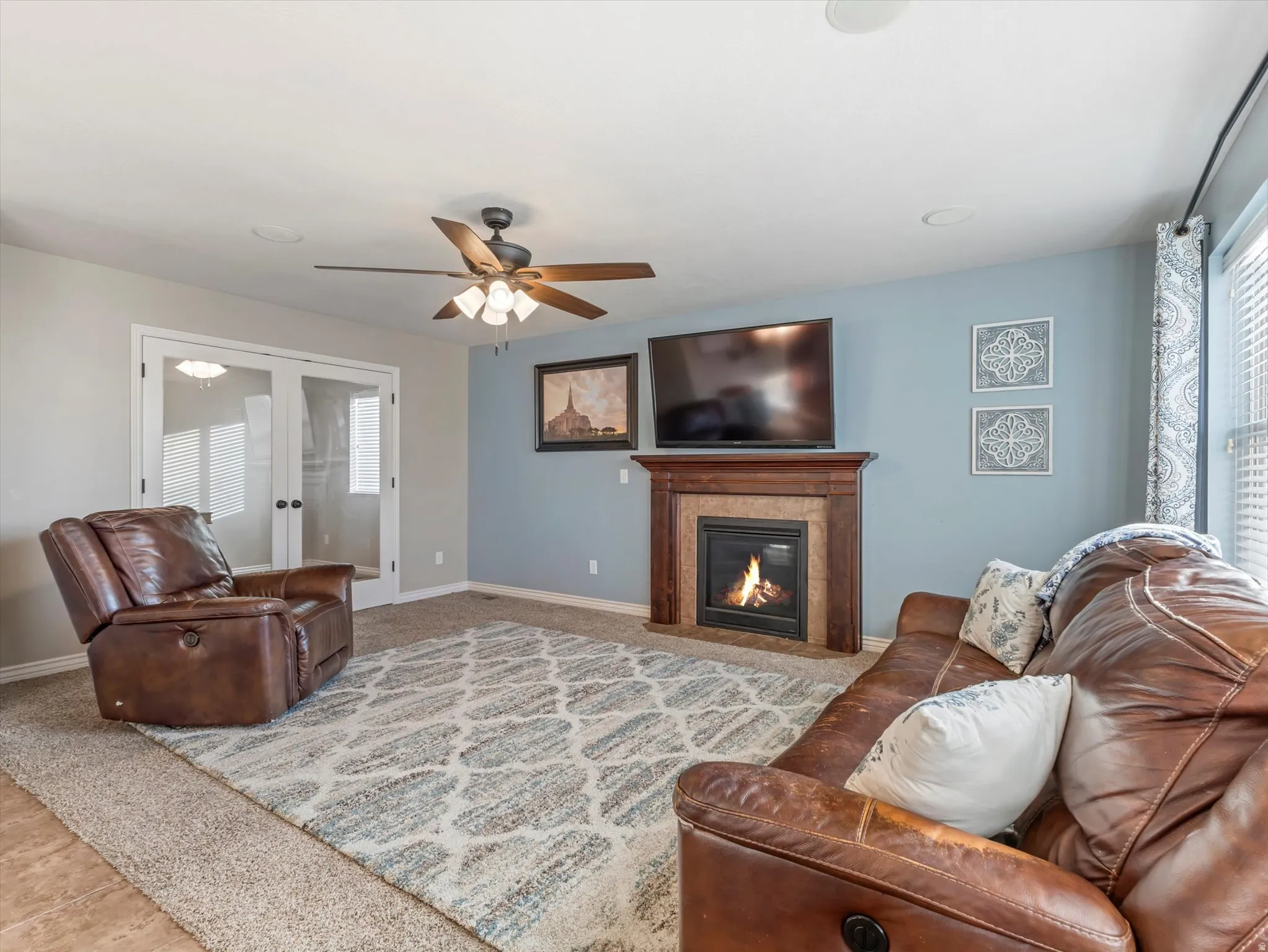 Carpeted living room with a fireplace with flush hearth, french doors, and a ceiling fan